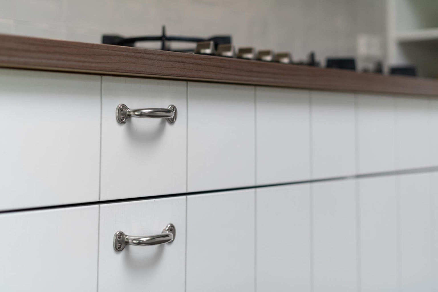 Detailfoto van greepjes op lades en deurtjes op landelijke, witte keuken op maat met ingefreesde frontjes om de aanblik van planken te creeeren.